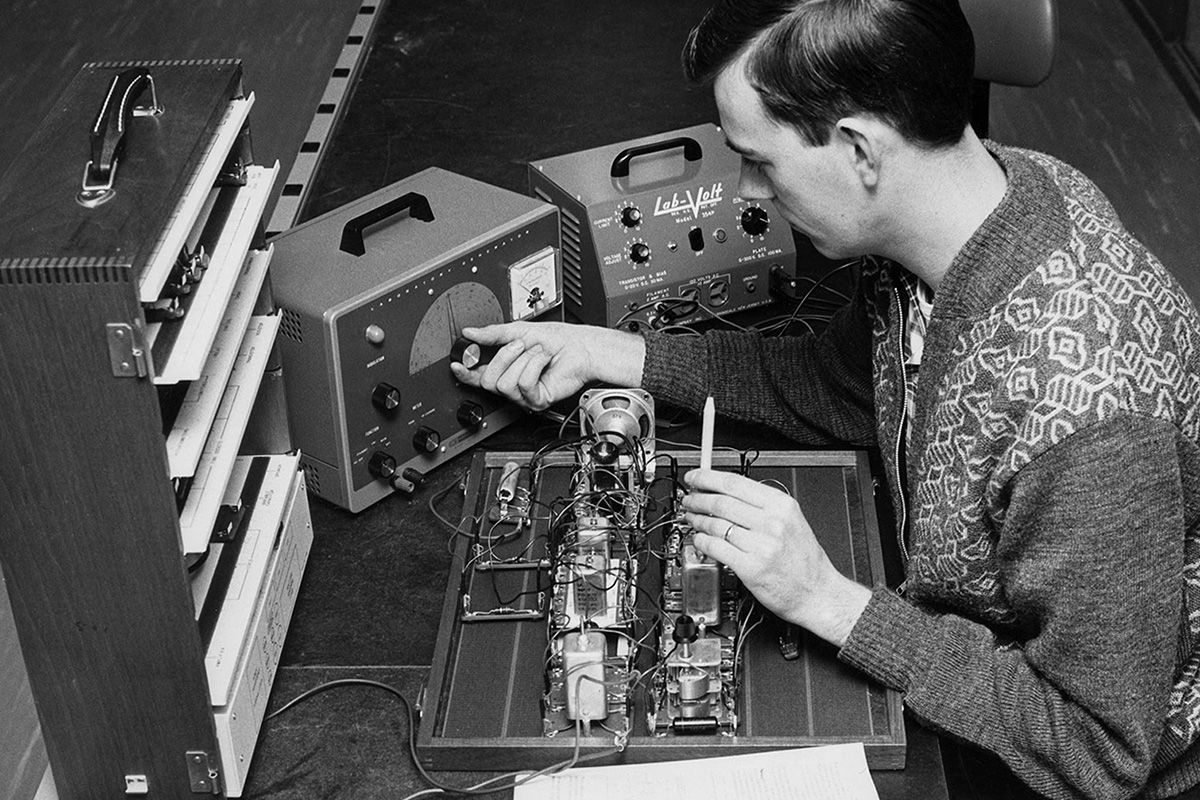 Student adjusting a laboratory generator and using a volt-meter while working on a piece of radio equipment