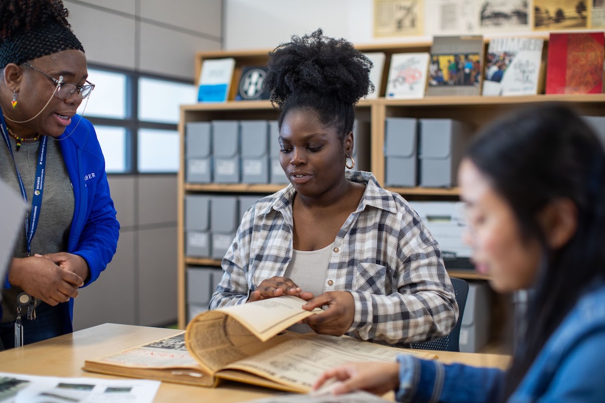 An Archives team member  showing two students photographs and books from the Humber Archives.