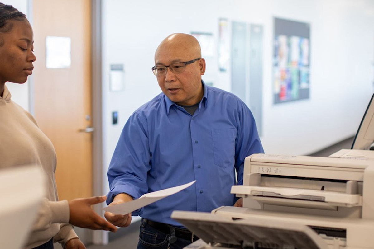 A Library team member helping a student use a Library printer. They are looking down at a piece of paper.